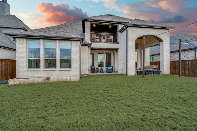 back of property at dusk featuring a balcony, a lawn, and brick siding