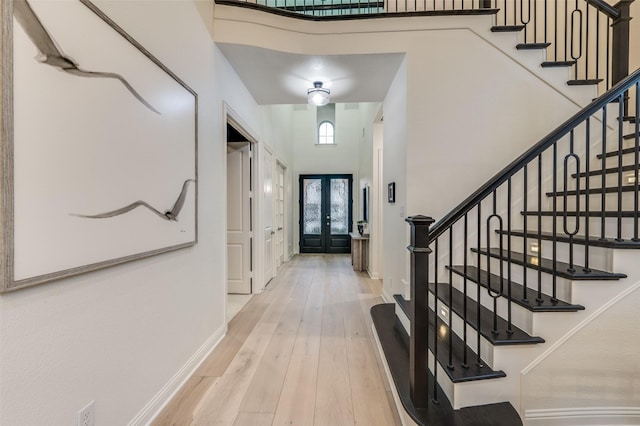 foyer entrance with hardwood / wood-style floors, baseboards, a high ceiling, stairs, and french doors