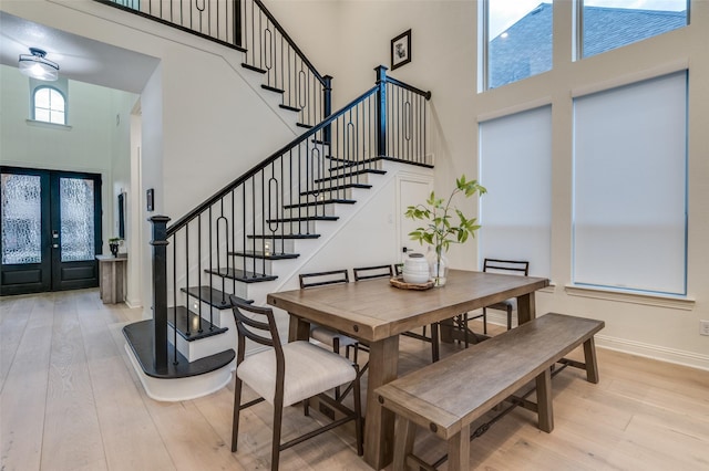 dining area featuring french doors, wood finished floors, a towering ceiling, and stairway