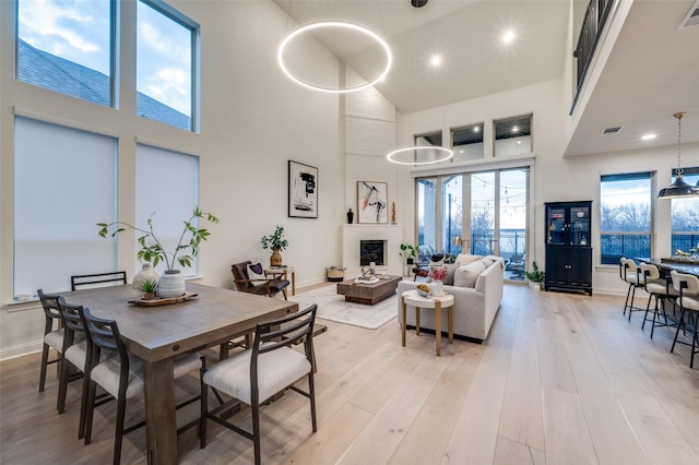 dining area featuring visible vents, light wood-style floors, a brick fireplace, and a towering ceiling