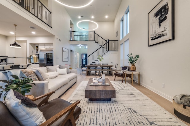 living room with stairway, baseboards, visible vents, a towering ceiling, and light wood-type flooring