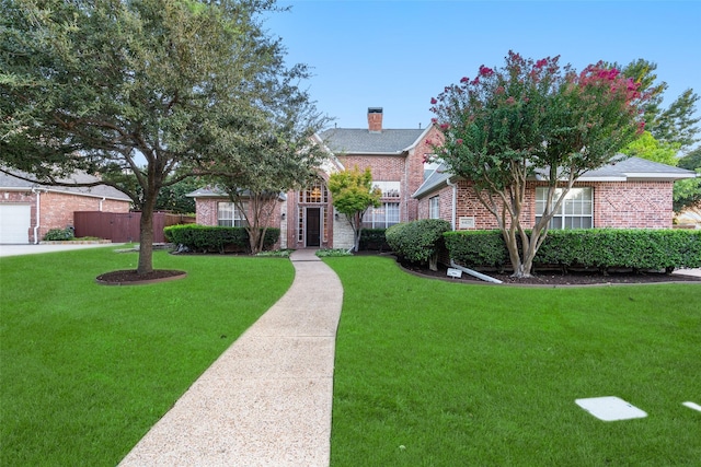 view of front of home with brick siding, a front lawn, a chimney, and fence