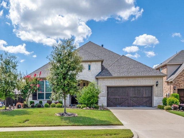 french country home featuring a garage, stone siding, concrete driveway, roof with shingles, and a front yard