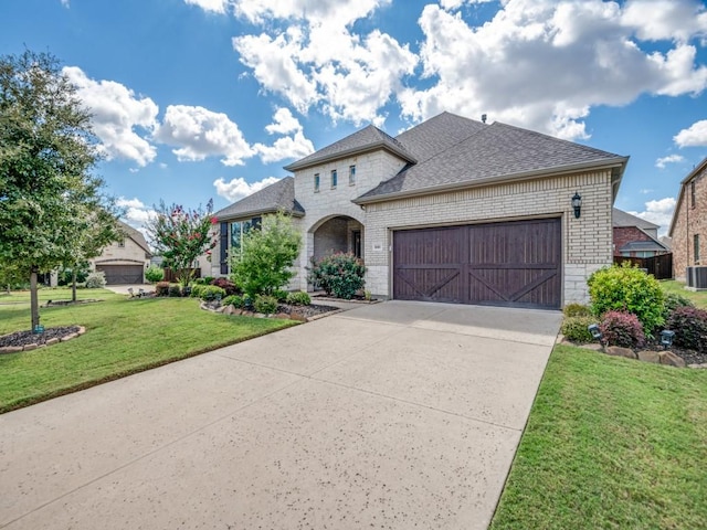 french country inspired facade featuring brick siding, a shingled roof, concrete driveway, an attached garage, and a front yard