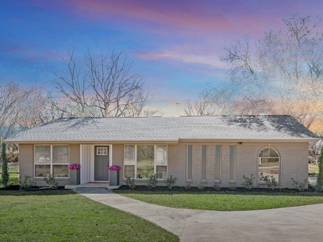 ranch-style house with brick siding, a front lawn, and roof with shingles