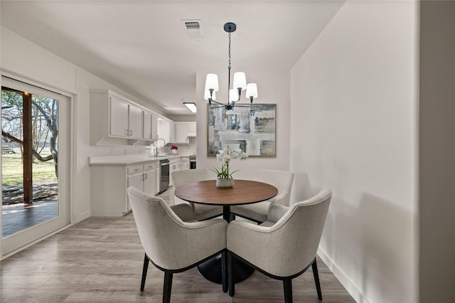 dining area featuring light wood-type flooring, visible vents, baseboards, and an inviting chandelier