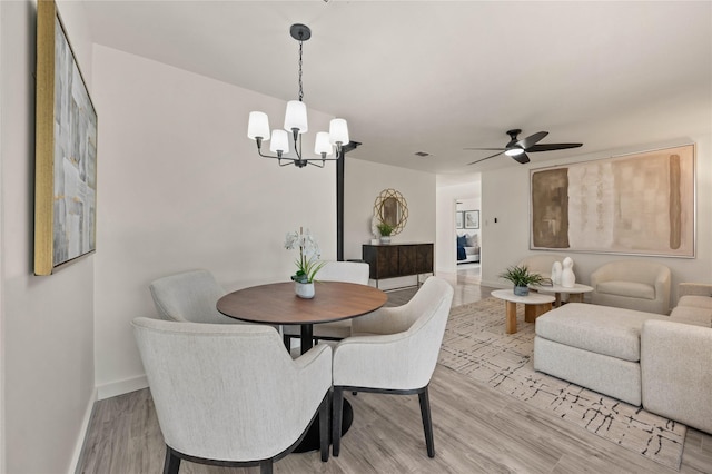 dining area with ceiling fan with notable chandelier, light wood-type flooring, visible vents, and baseboards