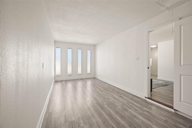 empty room with attic access, a textured wall, baseboards, and wood finished floors