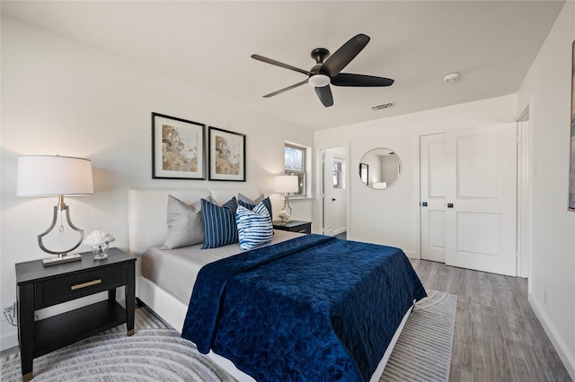 bedroom featuring ceiling fan, wood finished floors, visible vents, and baseboards