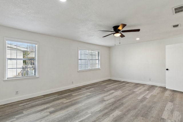 unfurnished room with visible vents, a textured ceiling, baseboards, and wood finished floors