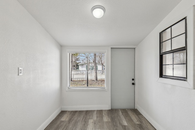 unfurnished room with a textured ceiling, baseboards, wood finished floors, and a textured wall