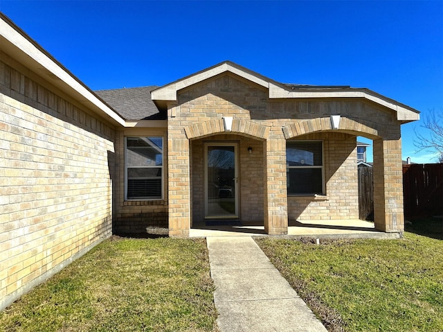 property entrance with a yard, roof with shingles, and brick siding