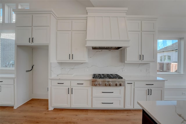 kitchen featuring white cabinetry, light wood-type flooring, custom exhaust hood, tasteful backsplash, and stainless steel gas stovetop