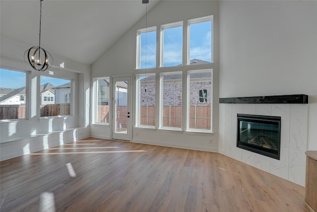 unfurnished living room with high vaulted ceiling, wood finished floors, a tile fireplace, and an inviting chandelier