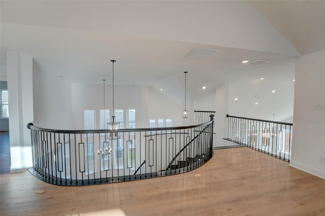 hallway with high vaulted ceiling, wood finished floors, an upstairs landing, visible vents, and an inviting chandelier