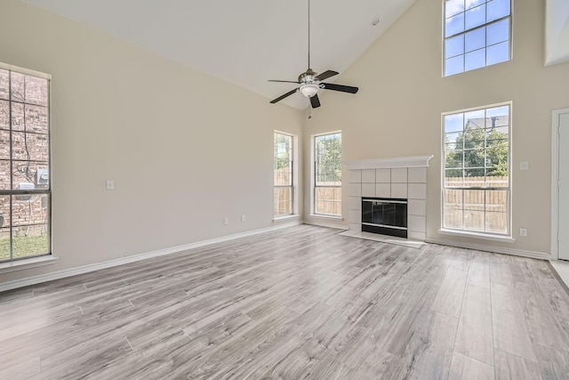 unfurnished living room featuring baseboards, high vaulted ceiling, a tile fireplace, and light wood-style floors