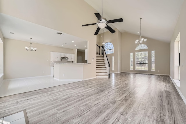 unfurnished living room with high vaulted ceiling, visible vents, light wood-style flooring, and ceiling fan with notable chandelier