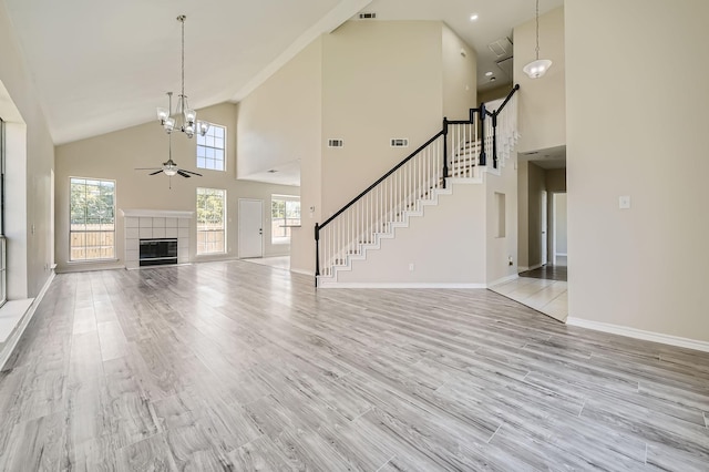 unfurnished living room featuring light wood-type flooring, a healthy amount of sunlight, stairway, and ceiling fan with notable chandelier