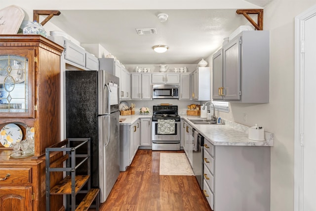 kitchen featuring dark wood-type flooring, a sink, visible vents, light countertops, and appliances with stainless steel finishes