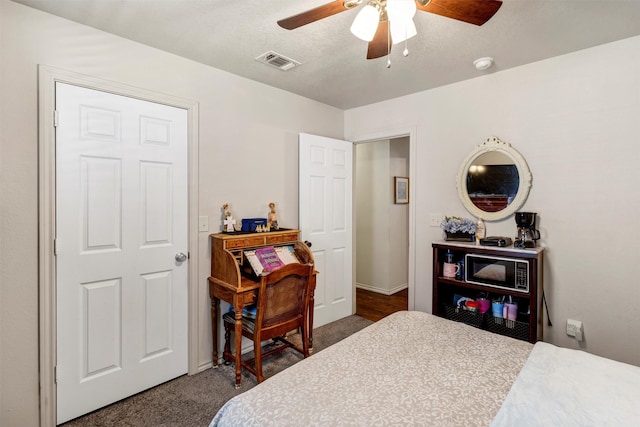 bedroom featuring a textured ceiling, dark carpet, visible vents, and a ceiling fan