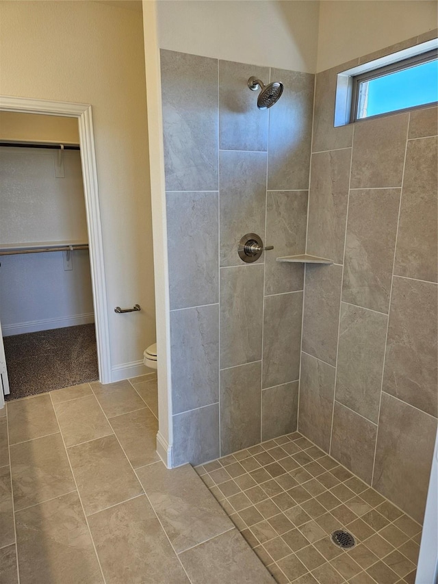 bathroom featuring a spacious closet, toilet, tiled shower, baseboards, and tile patterned floors