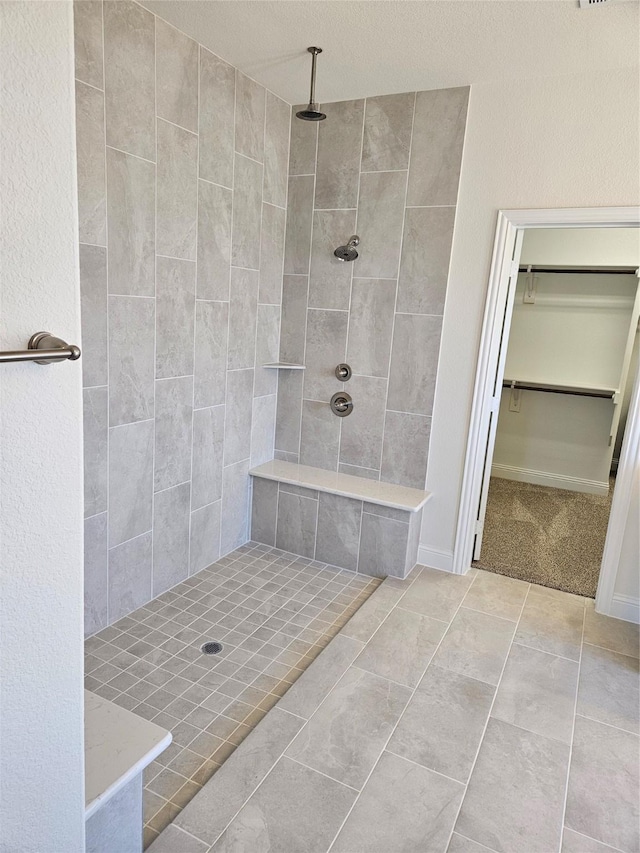 full bath featuring tiled shower, a walk in closet, and tile patterned floors