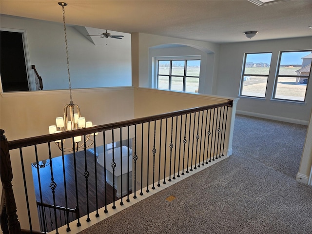 hall featuring a notable chandelier, baseboards, carpet flooring, and an upstairs landing