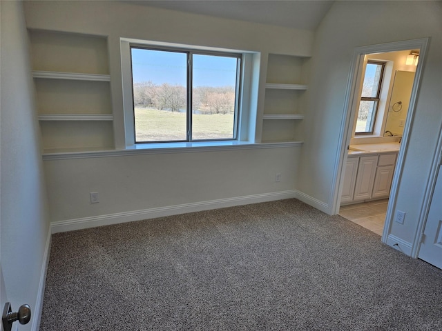 unfurnished bedroom featuring light carpet, baseboards, lofted ceiling, and ensuite bathroom