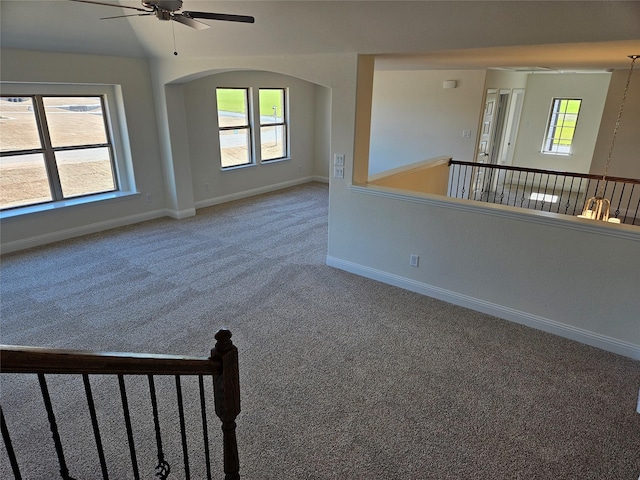 carpeted spare room with arched walkways, a ceiling fan, and baseboards