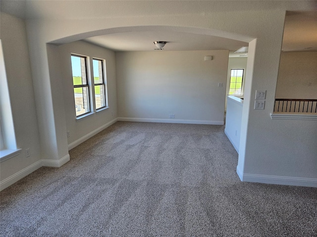 unfurnished room with arched walkways, carpet floors, a wealth of natural light, and baseboards