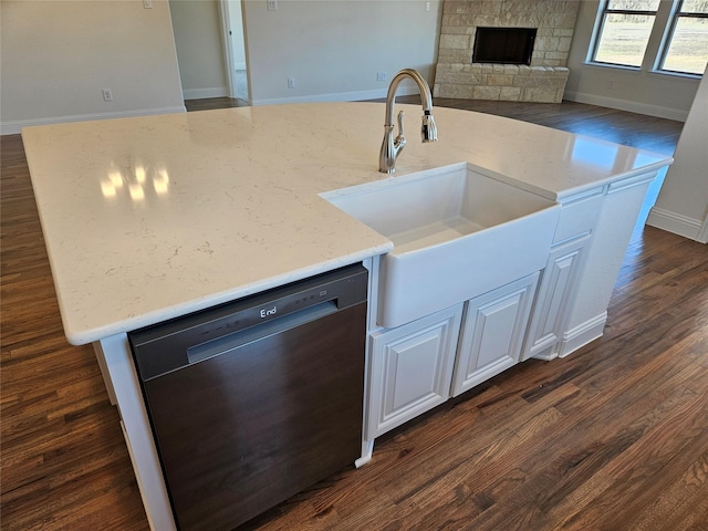 kitchen featuring dishwasher, light stone counters, dark wood-type flooring, a fireplace, and a sink