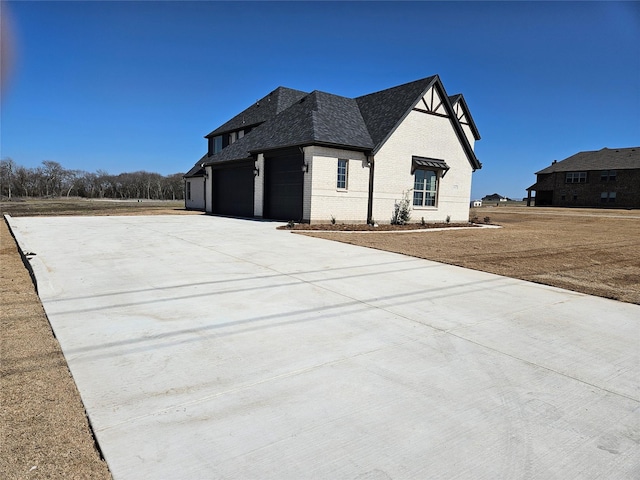 view of home's exterior with a shingled roof, concrete driveway, brick siding, and an attached garage