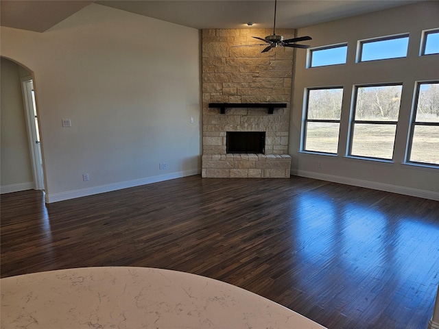 unfurnished living room featuring baseboards, arched walkways, a ceiling fan, dark wood-style flooring, and a fireplace