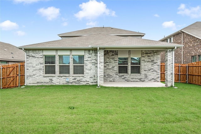 back of property with a fenced backyard, a yard, and brick siding