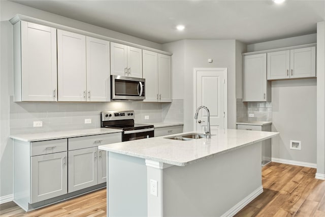 kitchen with a sink, baseboards, light wood-style floors, appliances with stainless steel finishes, and an island with sink