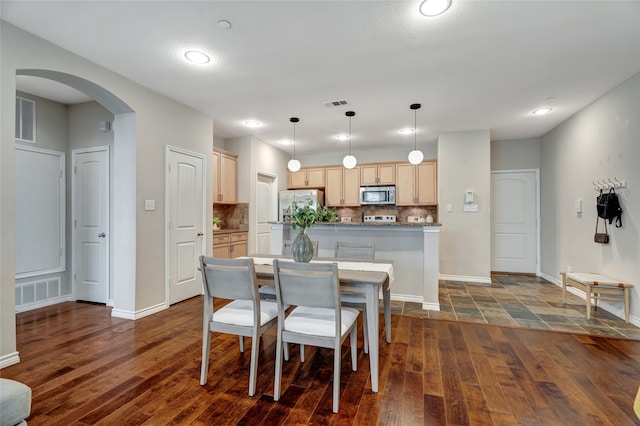 dining room with dark wood-style floors, visible vents, arched walkways, and baseboards