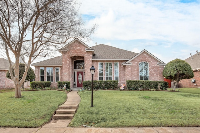 view of front facade with a shingled roof, brick siding, and a front lawn