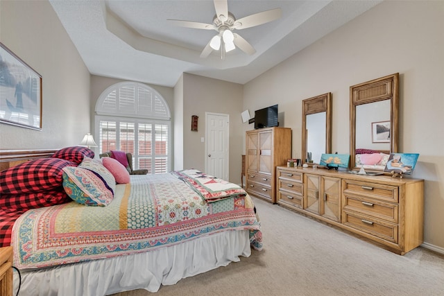 bedroom featuring light carpet, a tray ceiling, and a ceiling fan