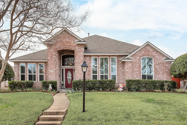 view of front facade featuring a shingled roof, a front lawn, and brick siding