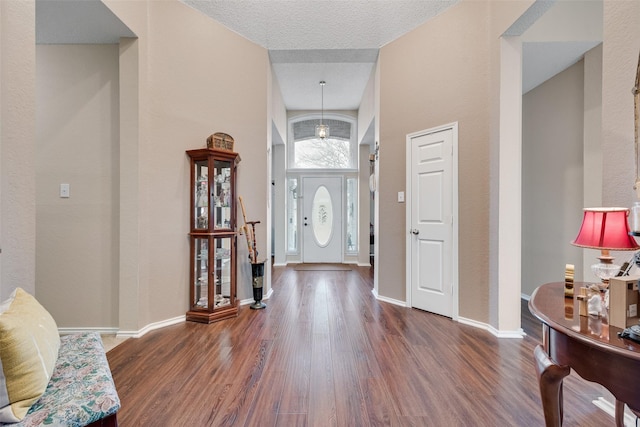 foyer featuring a towering ceiling, a textured ceiling, baseboards, and wood finished floors