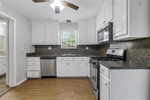 kitchen with stainless steel appliances, dark countertops, tasteful backsplash, light wood-style flooring, and white cabinets