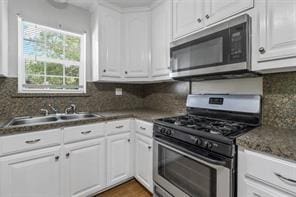 kitchen with wood finished floors, a sink, white cabinets, appliances with stainless steel finishes, and decorative backsplash