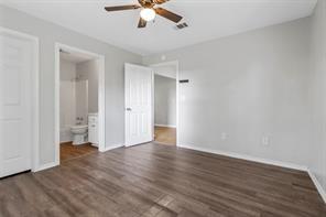 unfurnished bedroom featuring visible vents, ceiling fan, ensuite bath, wood finished floors, and baseboards