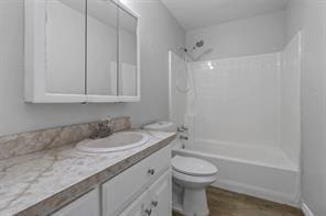 bathroom with toilet,  shower combination, wood finished floors, and vanity