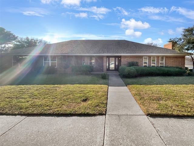 ranch-style home featuring brick siding, a chimney, a front yard, and a shingled roof