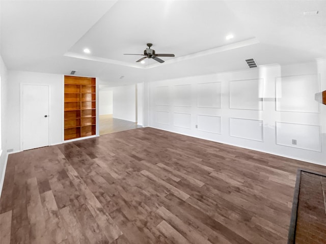 unfurnished living room featuring a tray ceiling, visible vents, a decorative wall, and wood finished floors