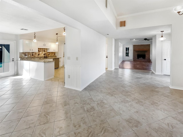 kitchen featuring a fireplace with raised hearth, a sink, a ceiling fan, open floor plan, and backsplash