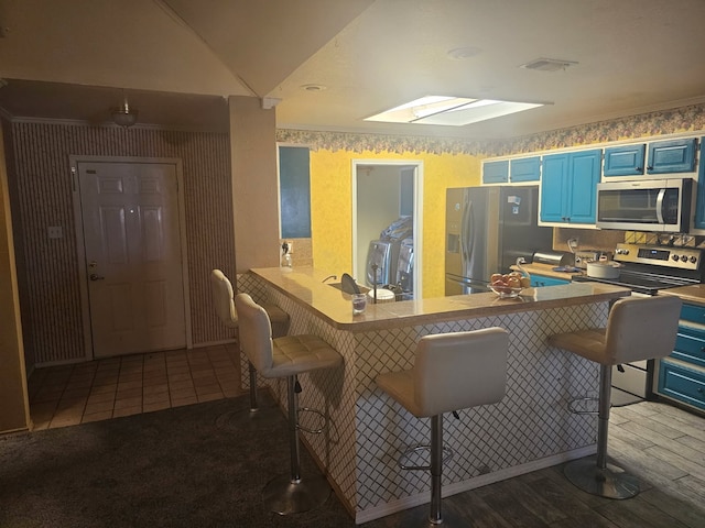 kitchen featuring a breakfast bar area, blue cabinetry, stainless steel appliances, visible vents, and vaulted ceiling