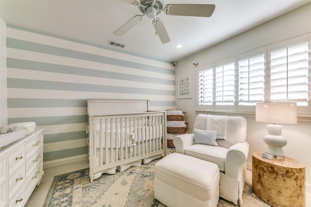 bedroom with visible vents, ceiling fan, a crib, baseboards, and wallpapered walls