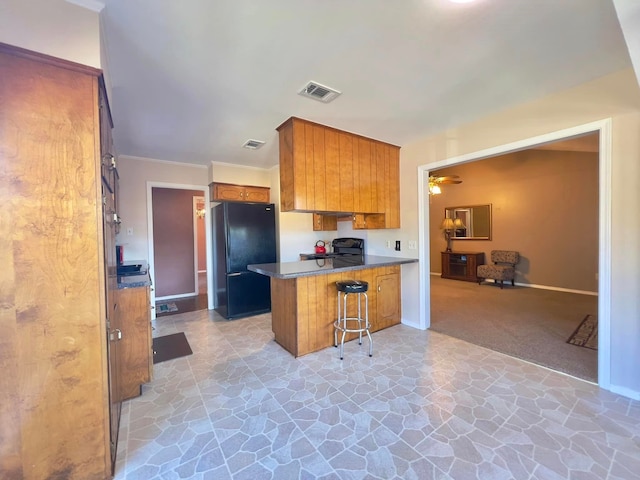 kitchen with a peninsula, visible vents, brown cabinetry, black appliances, and stone finish floor